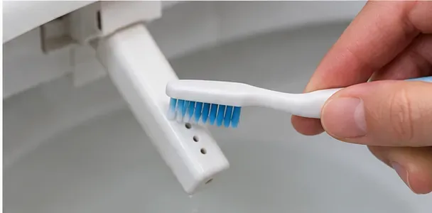 柔らかい歯ブラシを使って、延長型の白いビデノズルの吐水口を掃除している。
