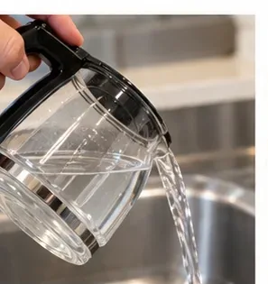 Gebruikt schoonmaakmiddel wordt vanuit een glazen koffiekan in de gootsteen gegoten.