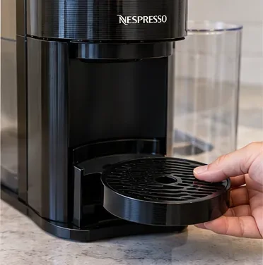 Hand die de kophouder verwijdert van een zwart Vertuo-achtig koffiezetapparaat.