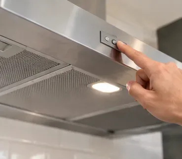 Een hand die een roestvrijstalen afzuigkap uitschakelt voordat de vetfilters worden verwijderd.