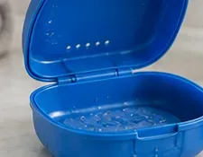 すすぎ後に水滴が見える、開いた状態の青いリテーナーケース。