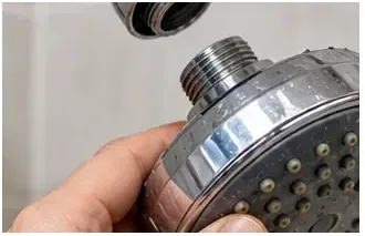 Een hand houdt een chromen douchekop vast, net nadat deze van de douchearm is losgeschroefd.