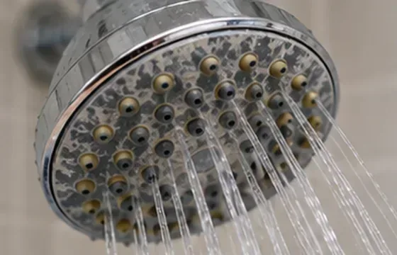 Een chromen douchekop met zichtbare witte kalkaanslag rond de sproeimondjes en een onregelmatige waterstraal.