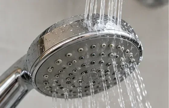 Een losse chromen douchekop wordt onder een krachtige straal schoon water bij de wastafel afgespoeld.