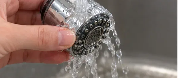 手がクロムメッキの蛇口ヘッドをきれいな流水で念入りにすすいでいる。