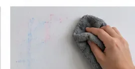 Een hand veegt voorzichtig met een zachte grijze microvezeldoek over de vage rode en blauwe vlekken.