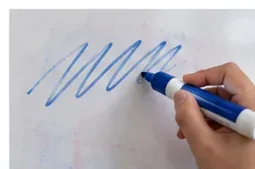Een hand die met verse blauwe whiteboardinkt rechtstreeks over vage, oudere markerresten op een whiteboard tekent.