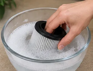 プリーツ状の掃除機用フィルターを、軽く石鹸水を張ったボウルの中で優しく洗浄している。