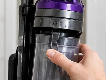メンテナンス前に、手が直立型掃除機からダストカップとフィルターハウジングを取り外している。