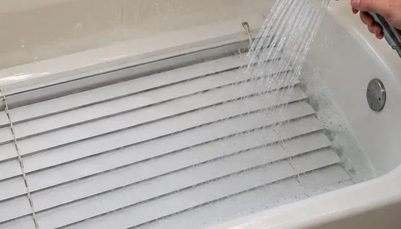 手持ちシャワーヘッドから出るきれいな水が、浴槽内の白い横型ブラインドの羽根を洗い流す。