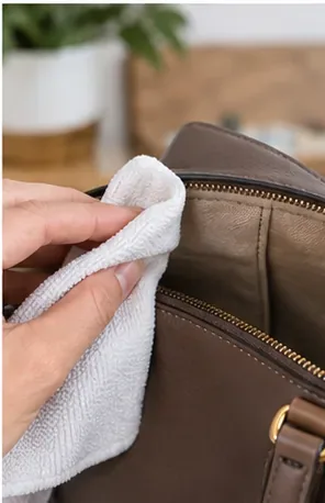 Een hand veegt de bruine leren afwerking aan de binnenkant van een handtas af met een schone witte doek.