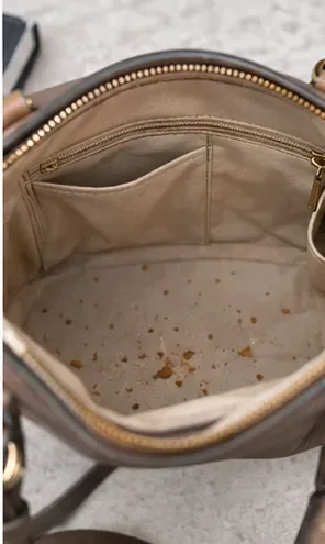 Een open handtas met kruimels en kleine vuiltjes verspreid over de lichte stoffen voering, vóór de schoonmaak.