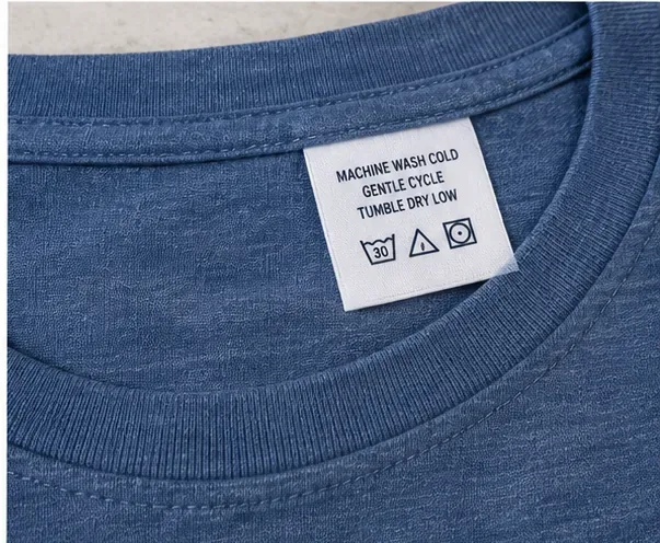 Close-up van een waslabel van een blauw overhemd met instructies voor machinewassen en drogen na vlekverwijdering.