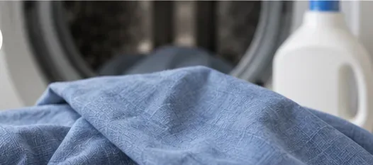 Een blauw kledingstuk wordt na een vlekverwijdering in een voorlader wasmachine geladen.