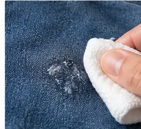 Met een schone witte doek dep je een klein vlekje kauwgomresten op een donkerblauwe spijkerbroek.