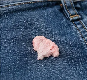 Roze kauwgom vastgeplakt aan donkerblauwe spijkerstof, vlakbij een naad.