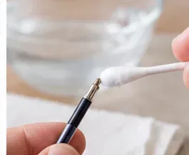 Een hand brengt voorzichtig een schoon wattenstaafje naar de blootliggende metalen punt van een penvulling.