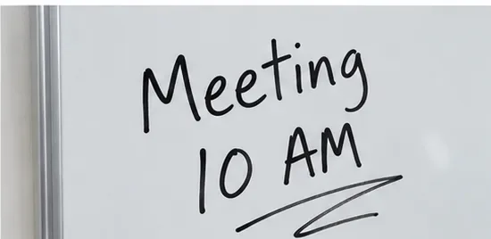 Met een zwarte watervaste stift wordt 'Vergadering 10:00 uur' op een wit whiteboard geschreven.