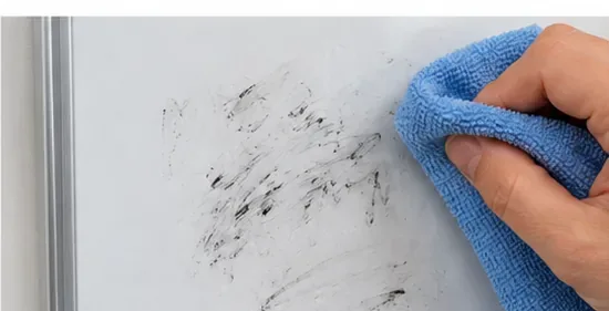 Een blauwe microvezeldoek veegt resten van een zwarte marker van een wit whiteboard.