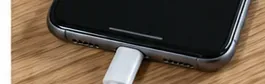 Зарядный кабель подсоединен к нижней части сухого смартфона на деревянной поверхности.