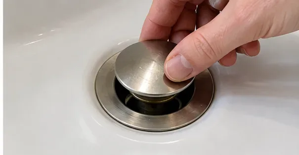 丸い金属製のシンクストッパーを排水口から持ち上げている手。
