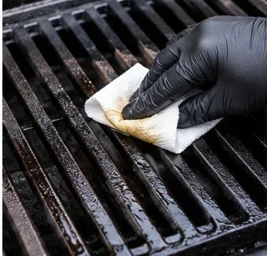 Met een gehandschoende hand wordt een zeer dun laagje olie over de gietijzeren grillroosters gesmeerd.