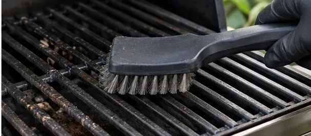 Een gehandschoende hand die vuil van het rooster van een gasbarbecue veegt.
