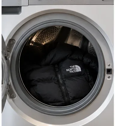 Een zwarte gewatteerde jas die losjes in de trommel van een wasmachine met voorlader ligt.