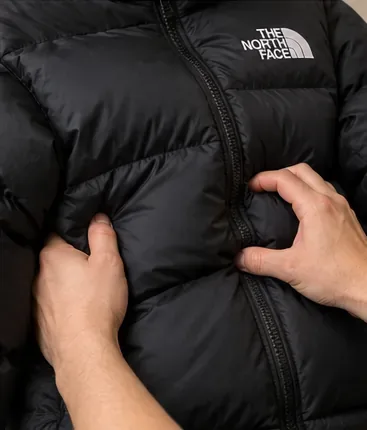 Met de handen worden de gewatteerde compartimenten van een zwarte gewatteerde jas zachtjes gemasseerd om de isolatie te herverdelen.