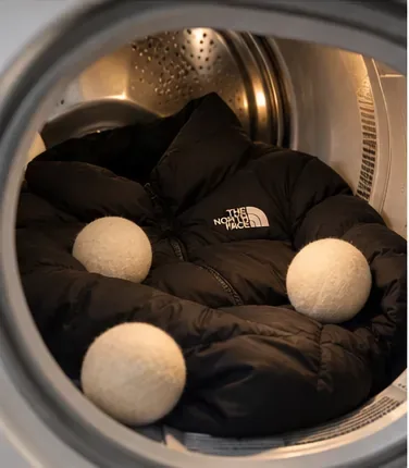 Een zwarte donsjas in een wasdroger met drie wollen droogballen.