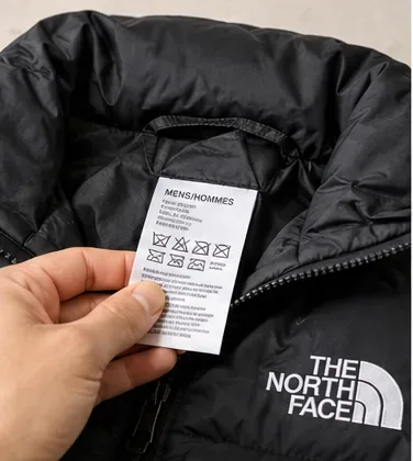 Een hand die het ingenaaide waslabel vasthoudt in een zwarte North Face-donsjas.