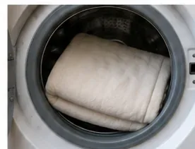 Een lichtgekleurde elektrische deken, losjes in een wasmachine met voorlader geplaatst, voor een zacht koud wasprogramma.