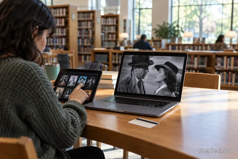 A library visitor selects a black-and-white film on a laptop beside a tablet and library shelves.