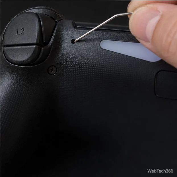 A paper clip pressing the small reset hole on the back of a DUALSHOCK 4 near the L2 button