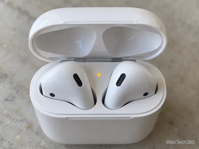 Visão aproximada de um estojo de carregamento dos AirPods aberto, com a luz indicadora âmbar entre os dois compartimentos dos fones de ouvido.