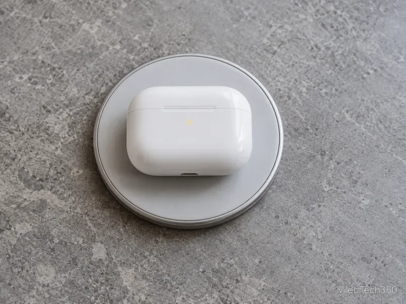 Estojo de carregamento dos AirPods branco fechado, apoiado em uma base de carregamento sem fio, com sua luz indicadora âmbar visível.